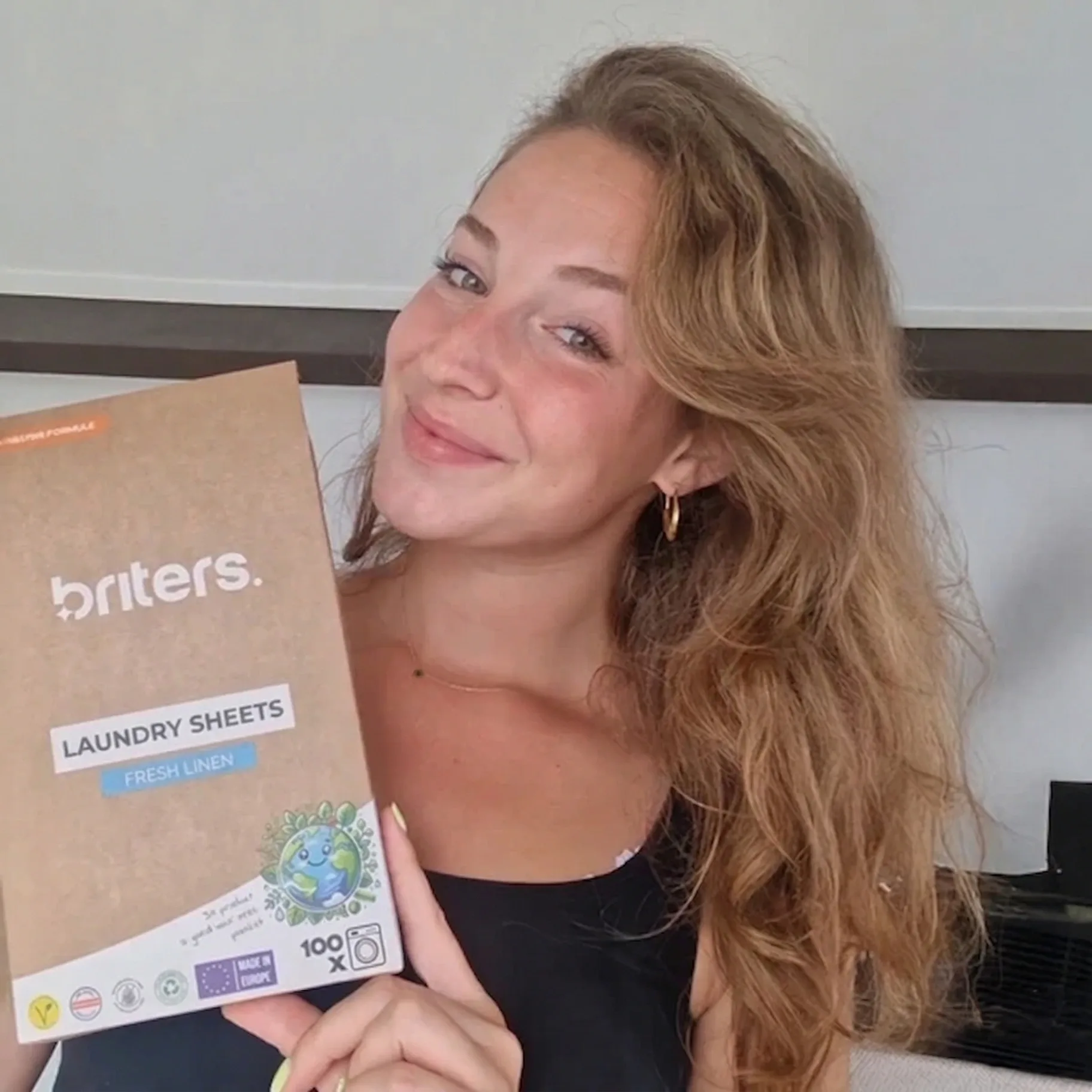 A smiling customer holds up a Briters Fresh Linen laundry sheets pack, 100 washes
