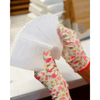 Gloved hands fanning out a stack of finished white Briters laundry sheets