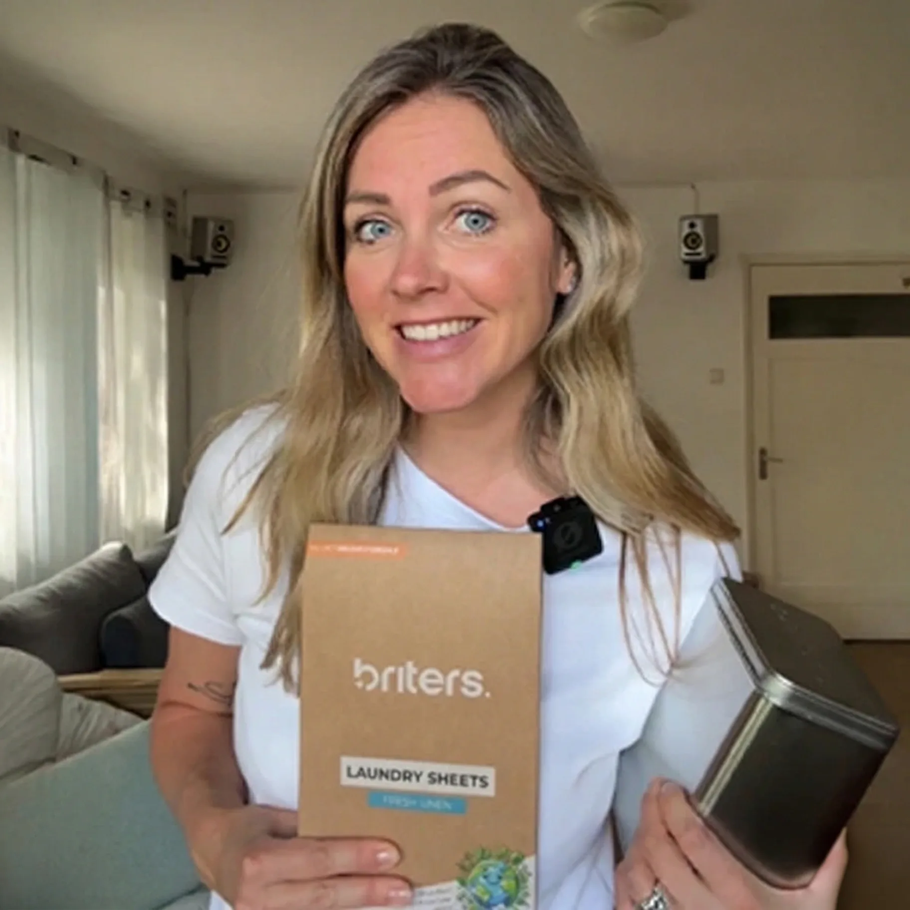 A customer in her living room holds a Briters Fresh Linen laundry sheets pack and a storage tin