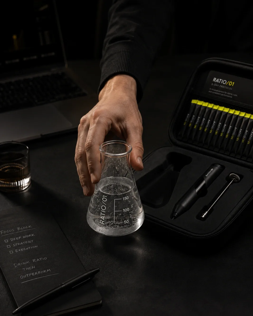 A hand lifting the mixed RATIO/01 glass from the desk beside the open kit